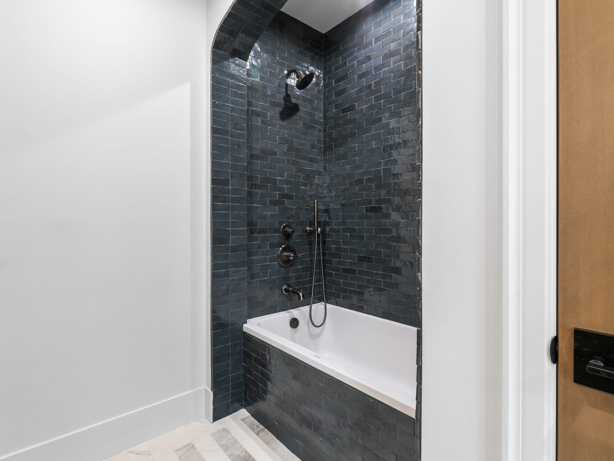 Arched tub and shower alcove in dark handmade Spanish tile with a deep soaking drop in tub, a tiled tub face, Kohler fixtures, and a marble heated floor in Happy Valley, OR