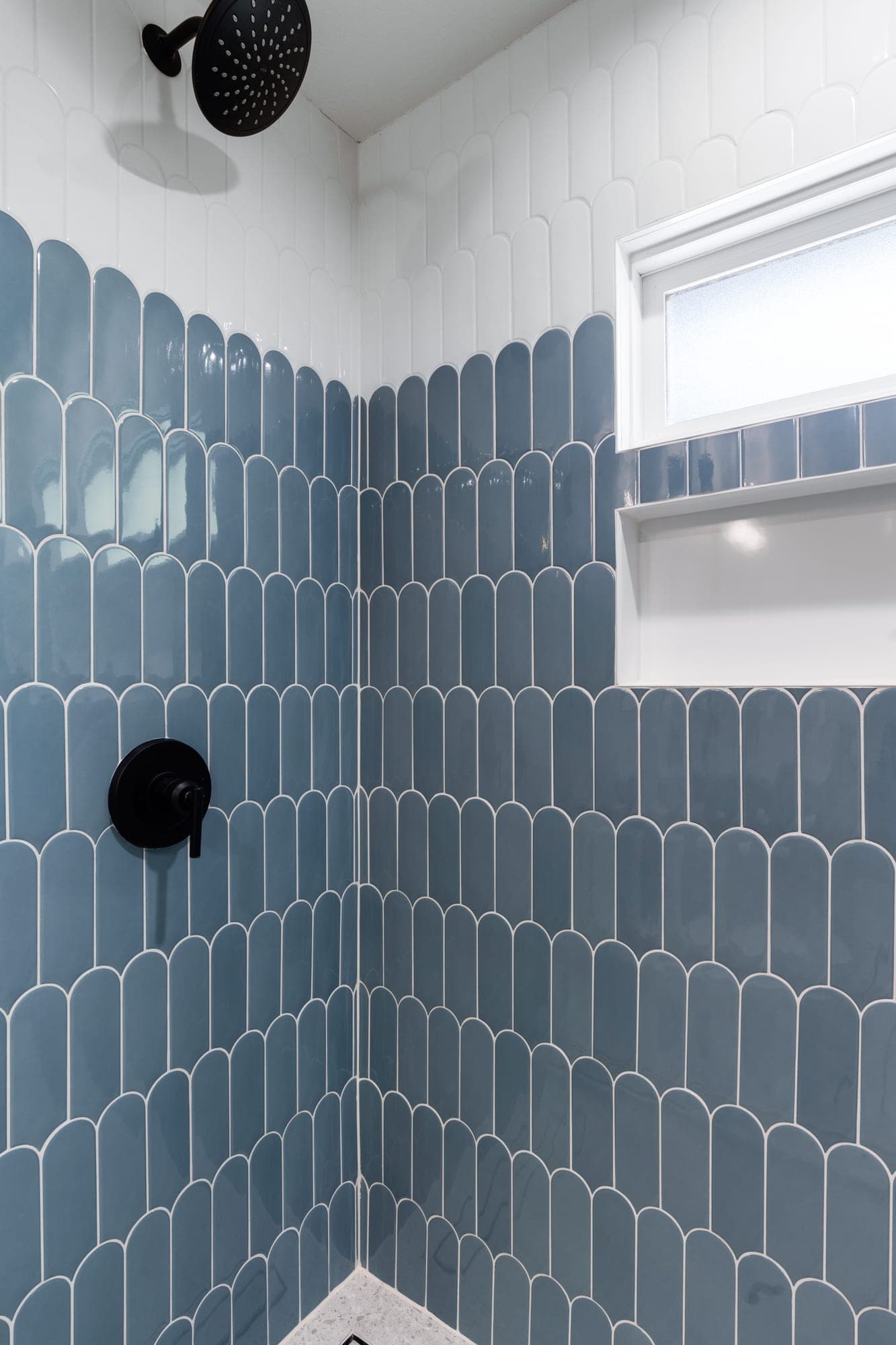 Matte black rain shower head and lever valve on blue fish scale tile below a white tile field in a craftsman shower in downtown Portland, OR