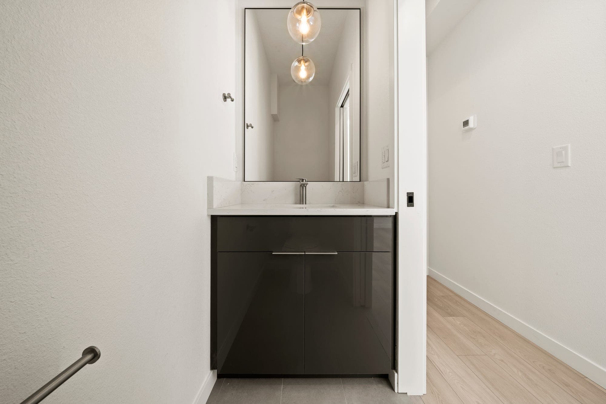 Powder bathroom with a dark high gloss vanity, a quartz counter and backsplash, a slim black framed mirror, glass globe pendants, and brushed nickel fixtures in Northeast Portland, OR