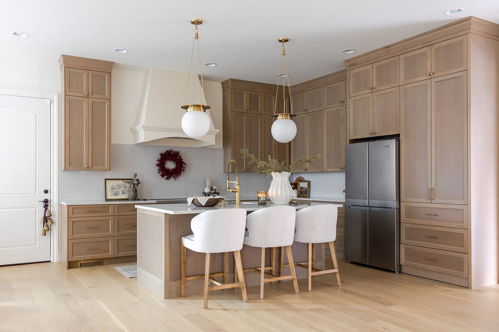 Custom white oak kitchen with a large island, a cream custom range hood, gold globe pendants, quartz counters, a full height quartz backsplash, and stainless steel appliances in Camas, WA