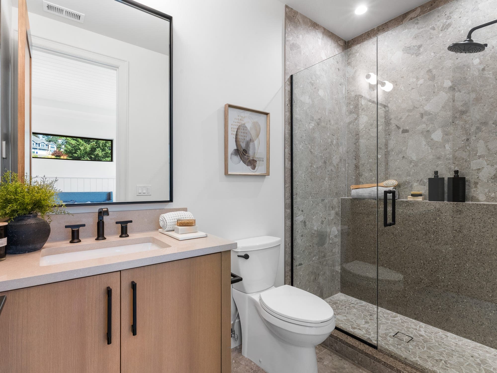 Walk in shower in large format terrazzo look tile with frameless glass beside a light wood vanity by Portland Tile in Portland, OR