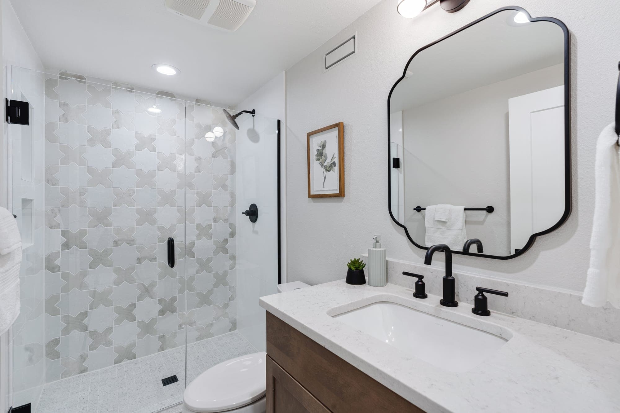 Walk in shower with star and cross pattern tile, frameless glass, and black fixtures after a tub to shower conversion by Portland Tile in Portland, OR