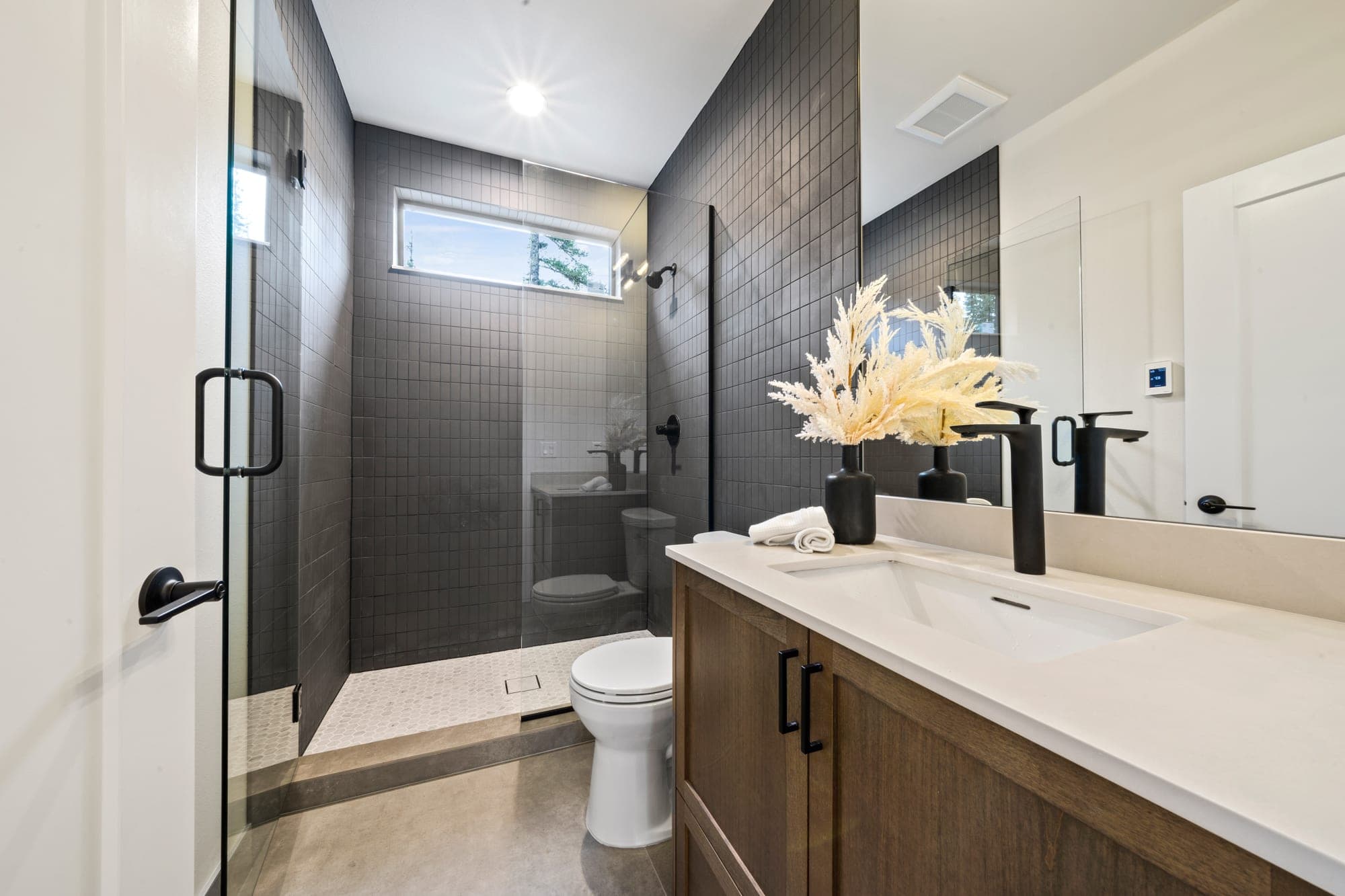 Walk in tile shower with charcoal stacked tile, a frameless glass door, a white mosaic pan, and a wood vanity with a quartz counter by Portland Tile & Remodels