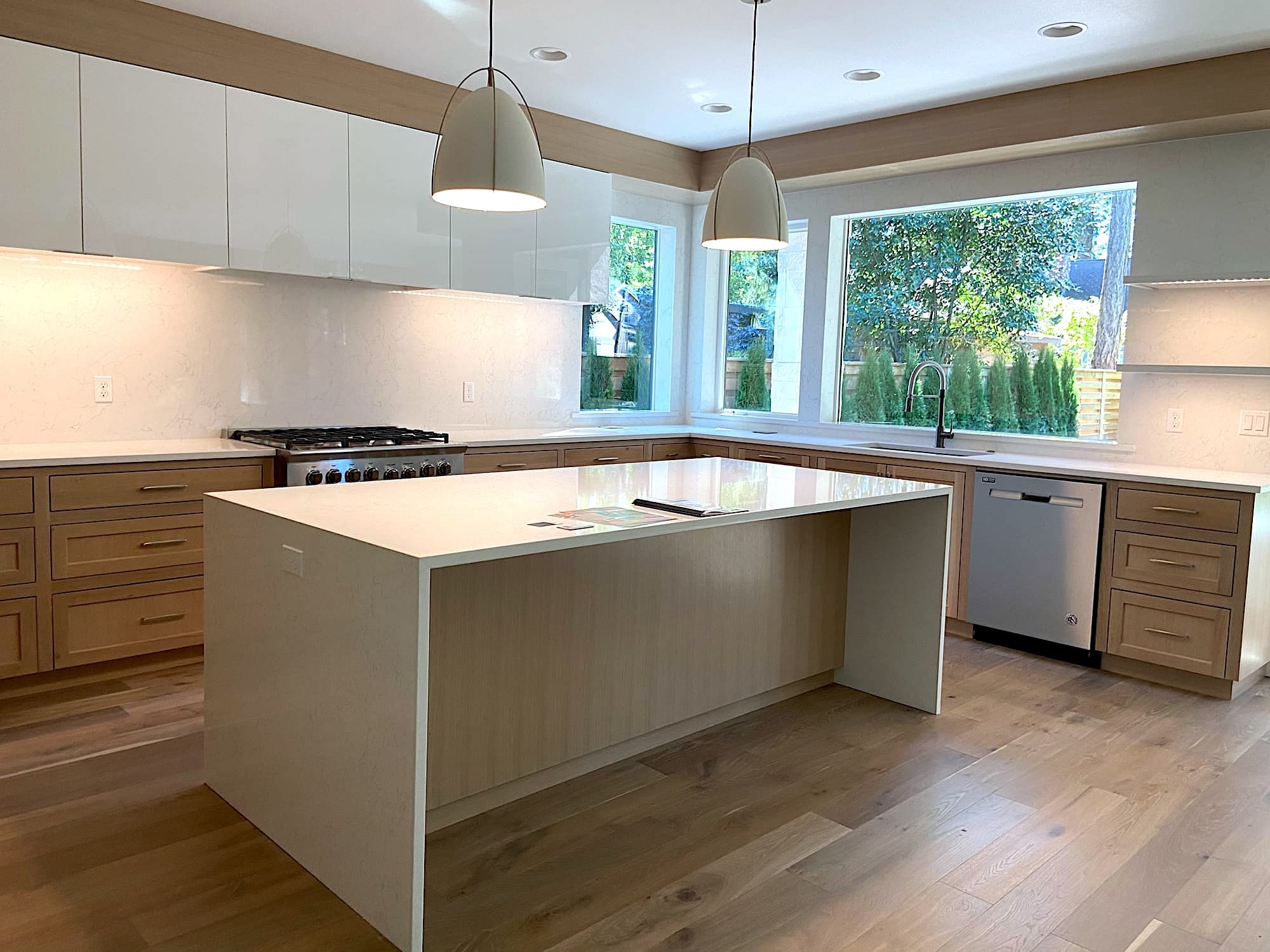Wide plank white oak hardwood flooring running through an open kitchen with a large island and light wood cabinetry by Portland Tile & Remodels