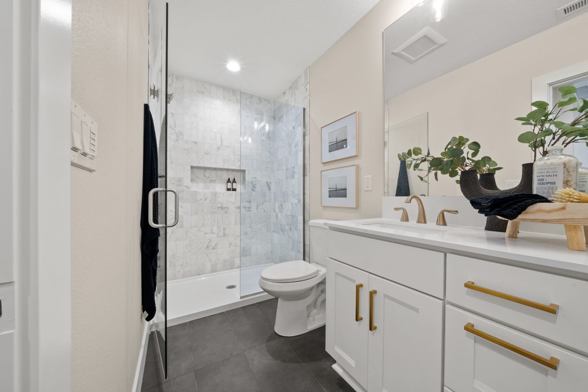 Primary bathroom with a marble tile shower, frameless glass, a custom niche, dark tile floor, and gold fixtures in Southwest Portland, OR