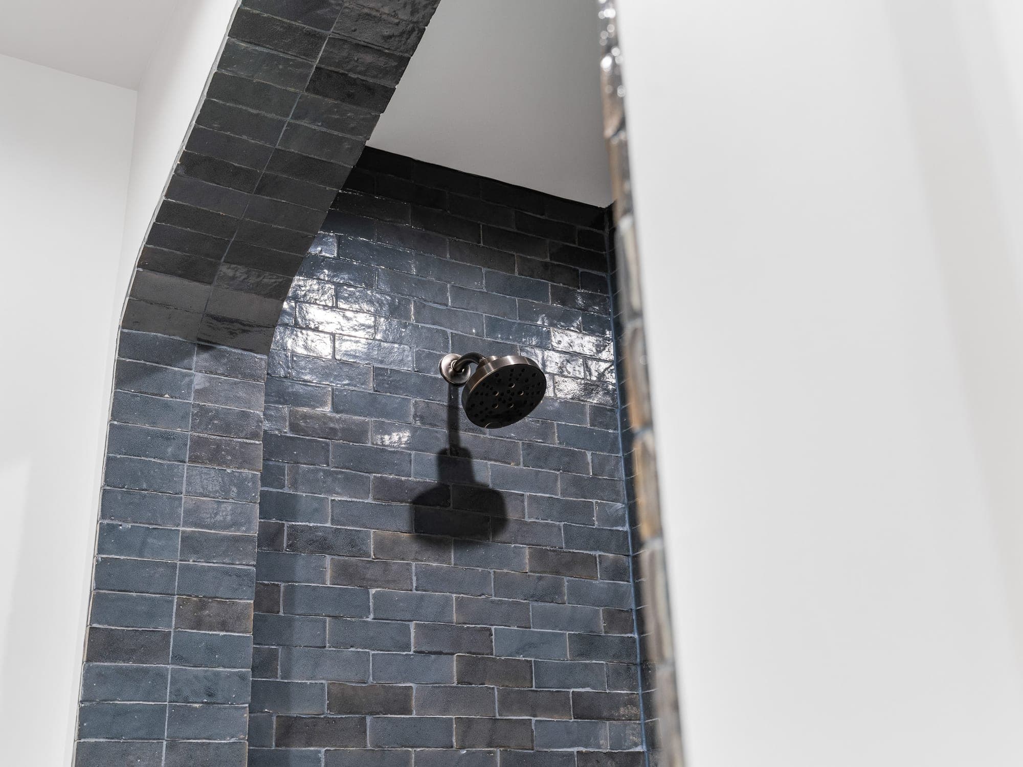 Detail of dark handmade Spanish tile wrapping the arch of a shower alcove with a Kohler shower head in Happy Valley, OR