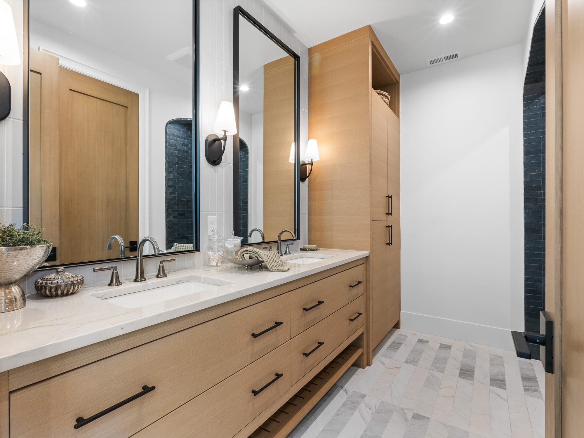 Custom white oak double vanity with a quartz counter, a full height tile backsplash to the ceiling, black framed mirrors mounted over the tile, wall sconces, a linen closet on the end, and a heated marble floor in three tones in Happy Valley, OR