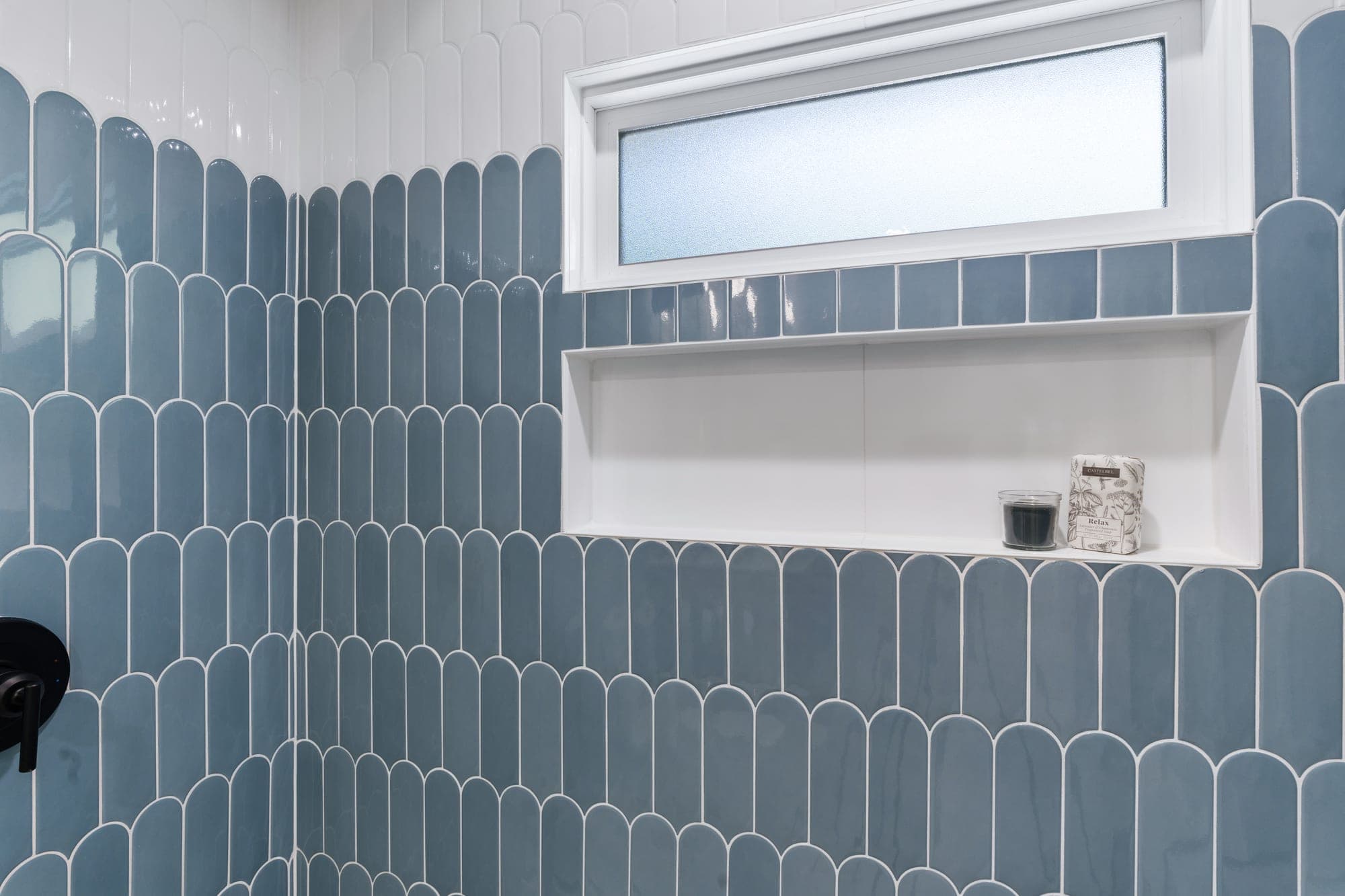 Large custom shower niche and obscured glass window finished with an aluminum edge, framed by blue and white fish scale tile in downtown Portland, OR