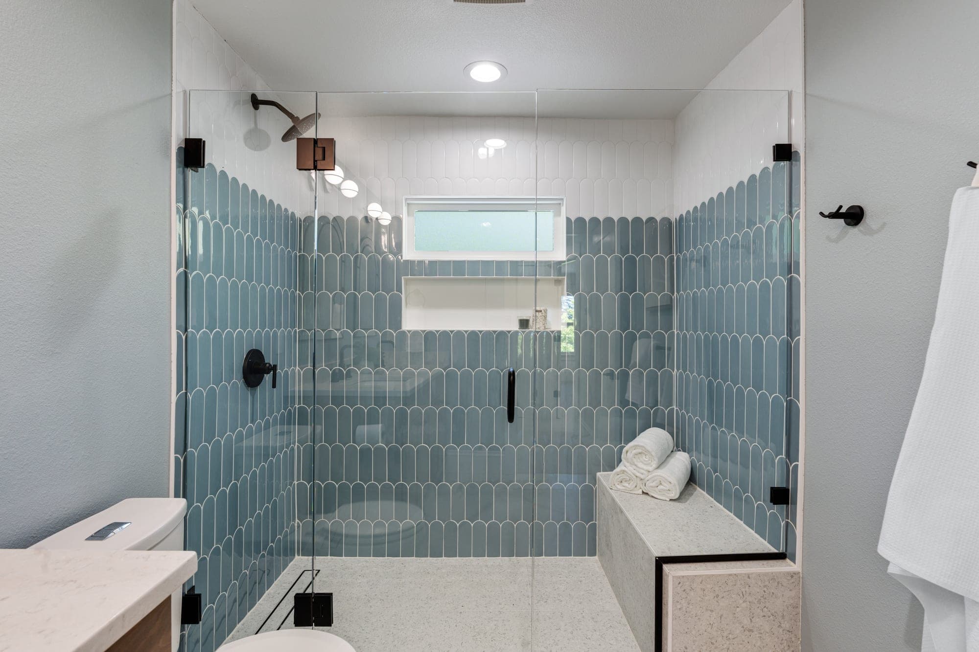 Walk in shower with blue and white fish scale wall tile, frameless glass, a terrazzo bench, and an obscured glass window in downtown Portland, OR