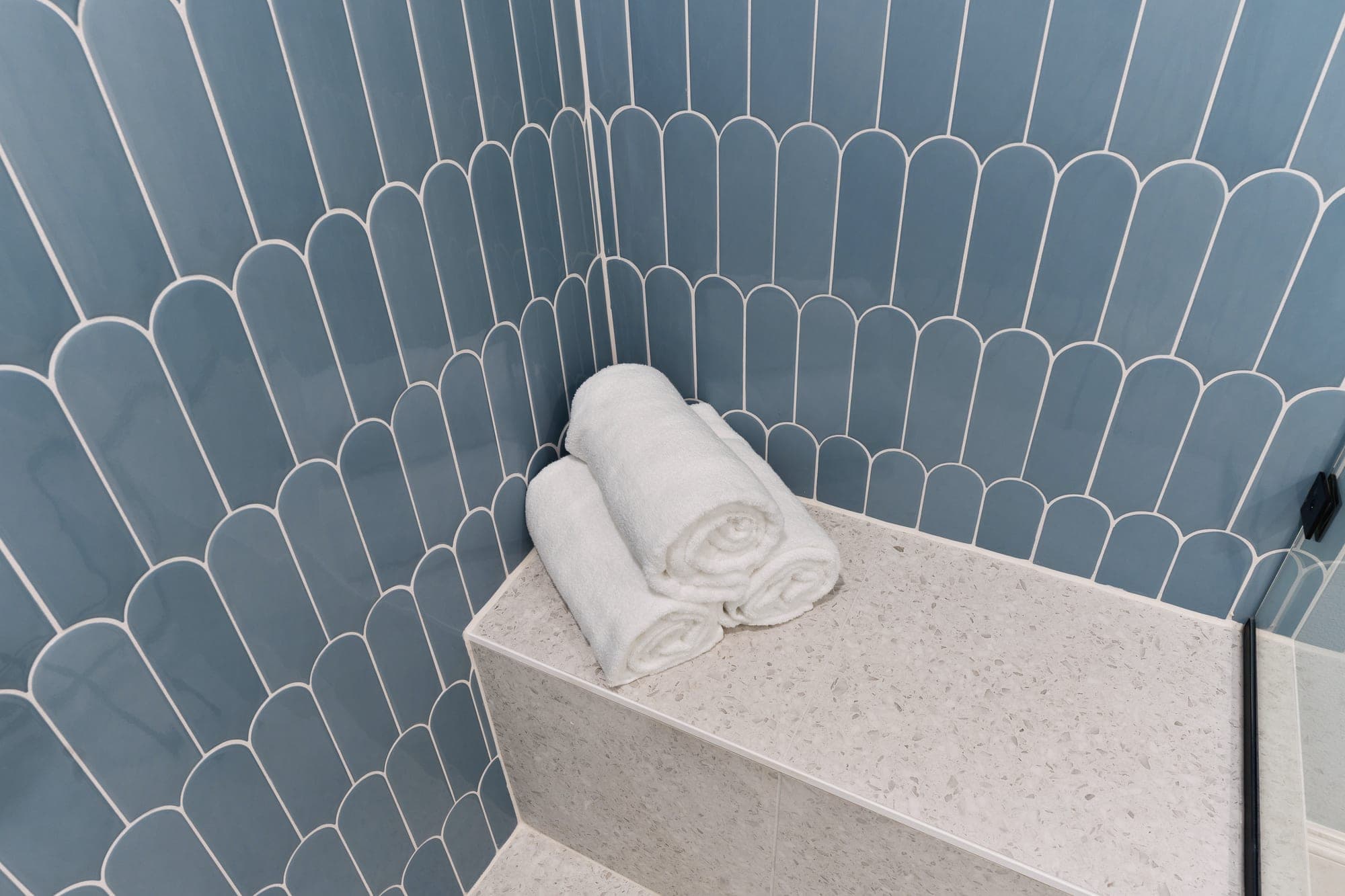 Terrazzo shower bench with rolled white towels against blue and white fish scale tile in downtown Portland, OR