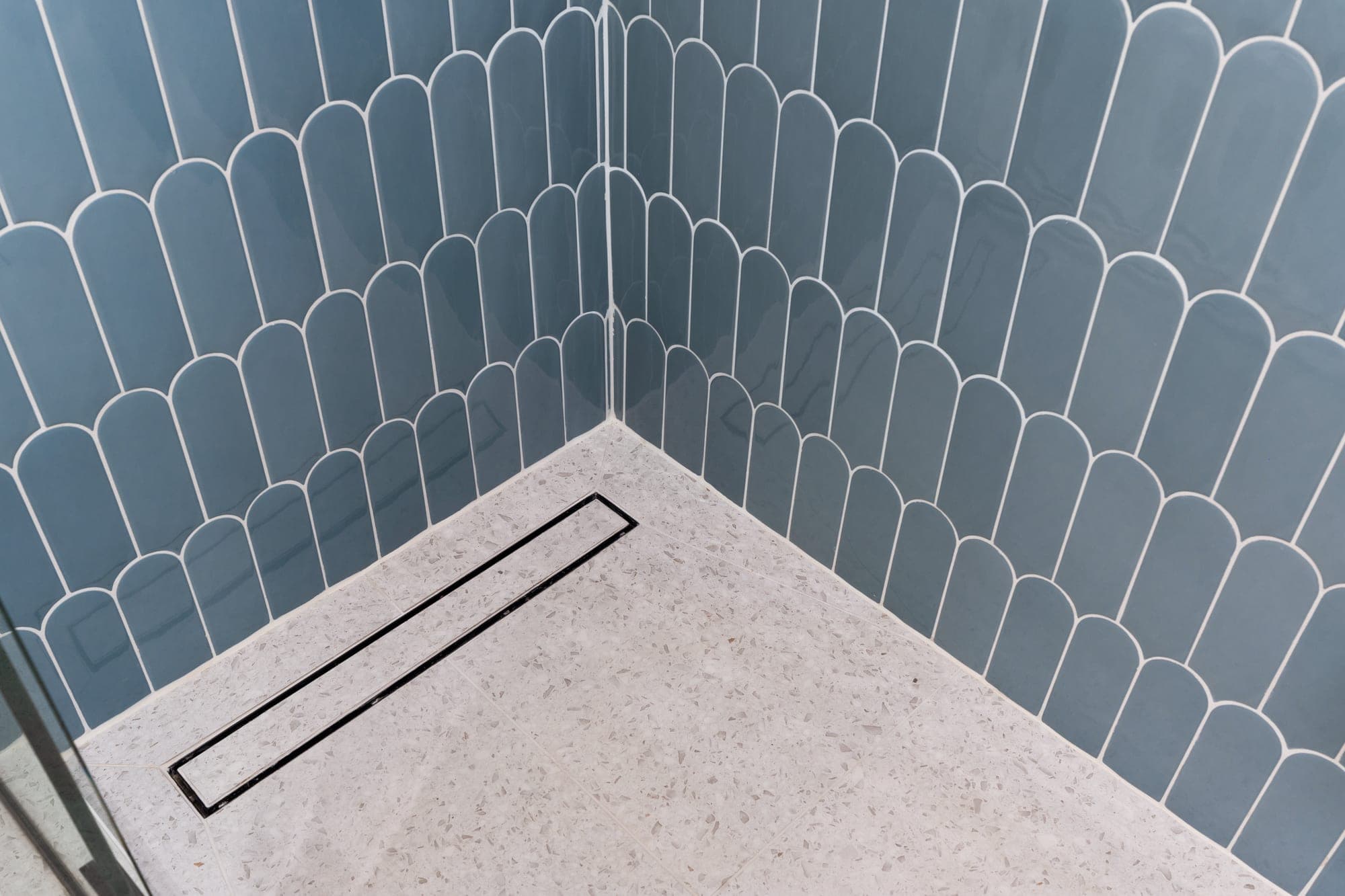 Terrazzo shower pan with a linear drain whose cover is set in the same terrazzo tile, meeting blue fish scale walls in downtown Portland, OR