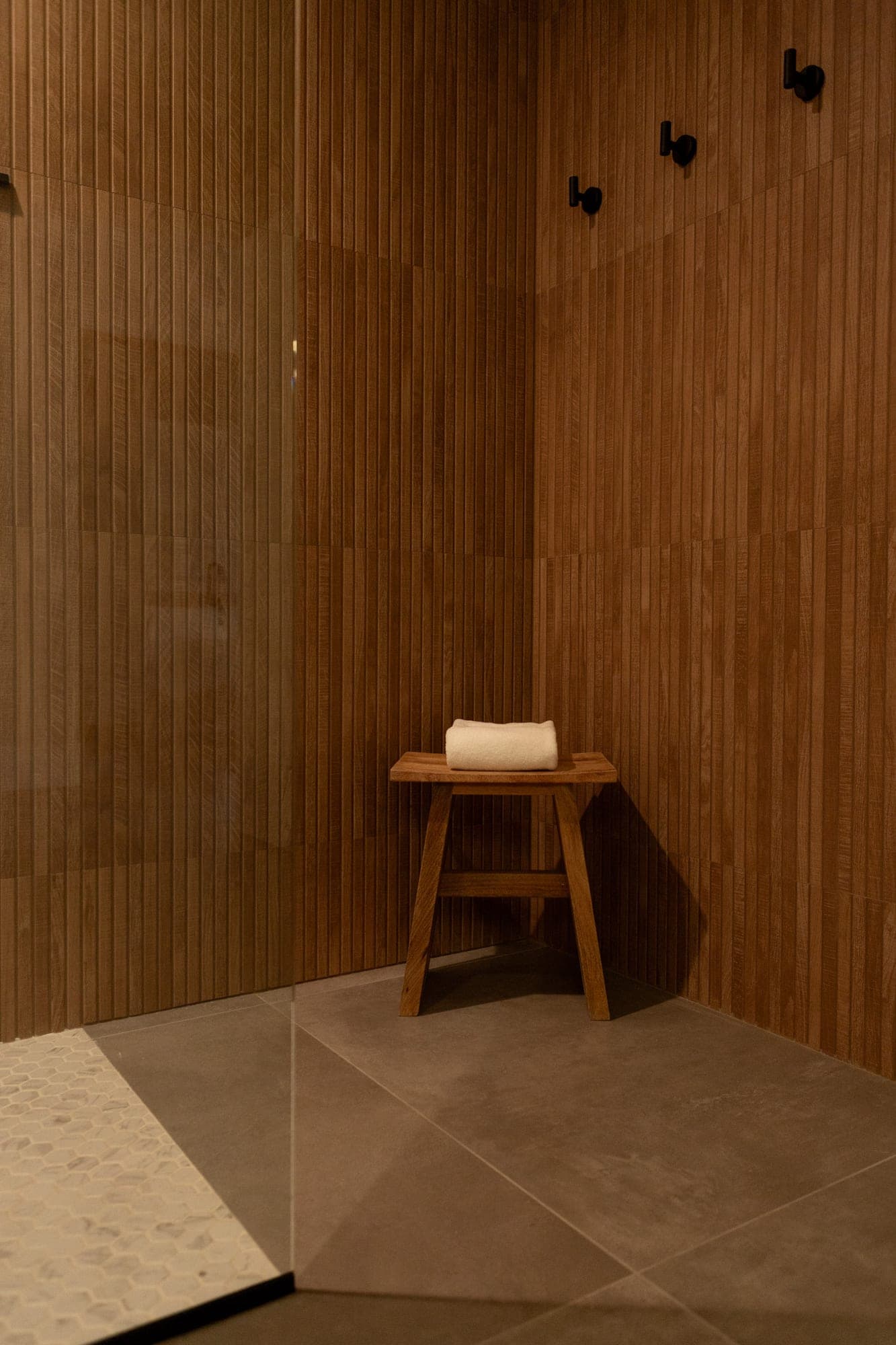 Moody shower corner with fluted wood look tile, a teak stool, and black hooks in Government Camp, OR