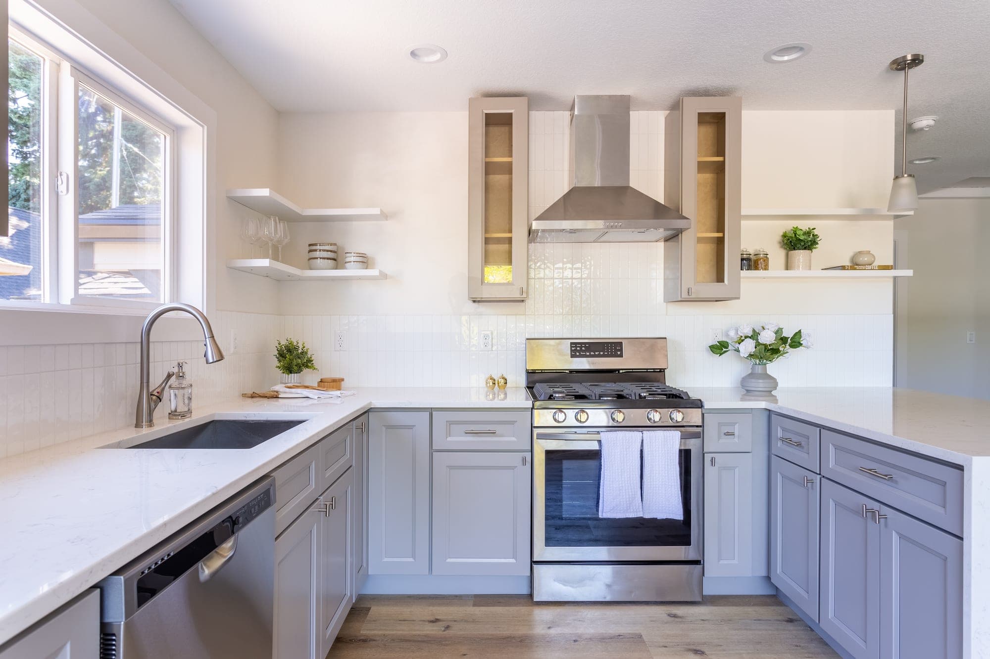 Remodeled kitchen with gray ready to assemble shaker cabinets, quartz counters, white vertical stacked tile backsplash, floating shelves, and stainless steel appliances in Hillsboro, OR