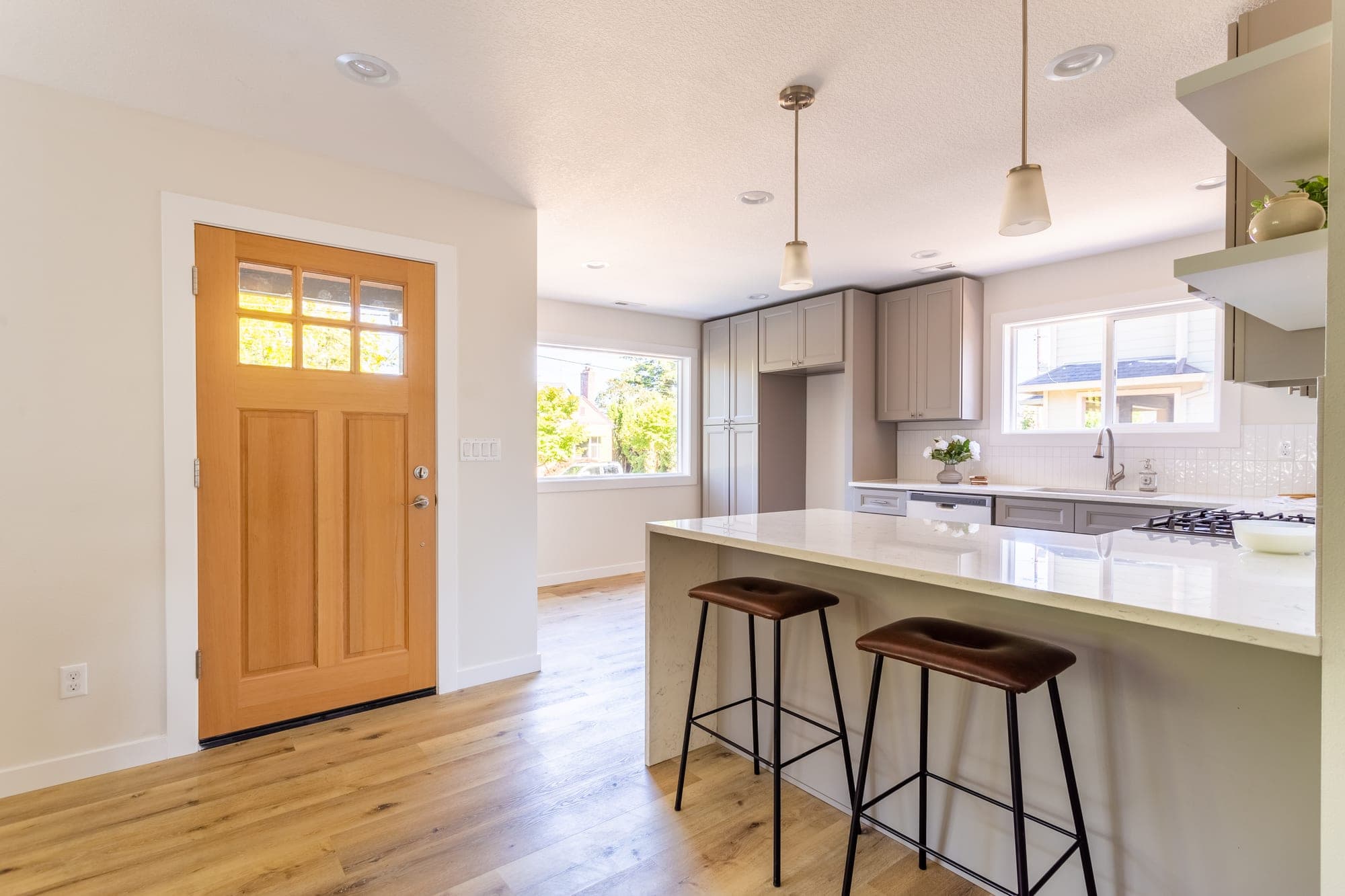 Open concept kitchen with a large peninsula and a waterfall quartz countertop where a wall to the living room was removed, with luxury vinyl plank flooring in Hillsboro, OR
