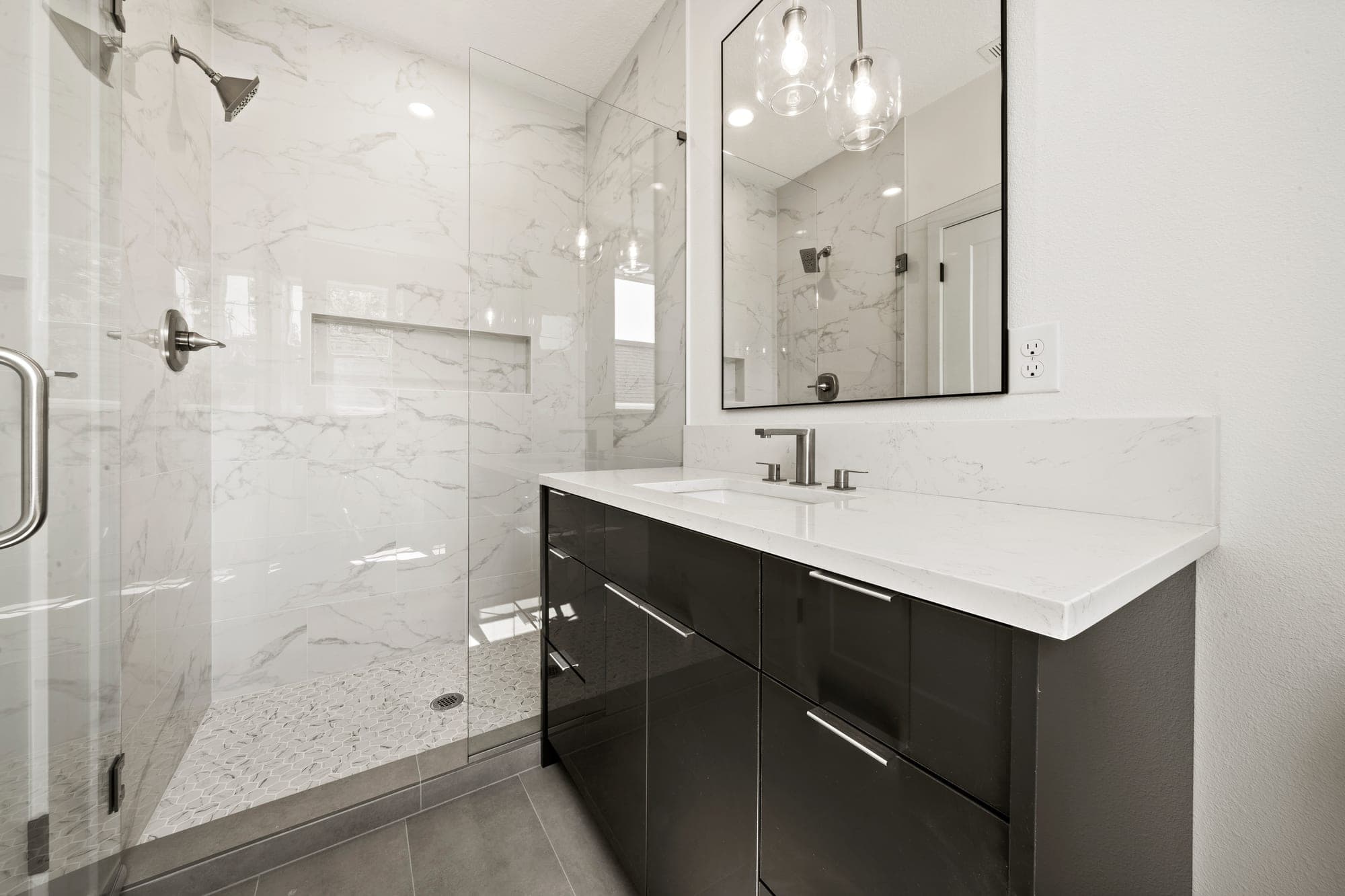 Modern primary bathroom with a white marble tile shower, frameless glass, a marble hexagon mosaic shower pan, a dark high gloss vanity, a quartz counter, and brushed nickel fixtures in Northeast Portland, OR