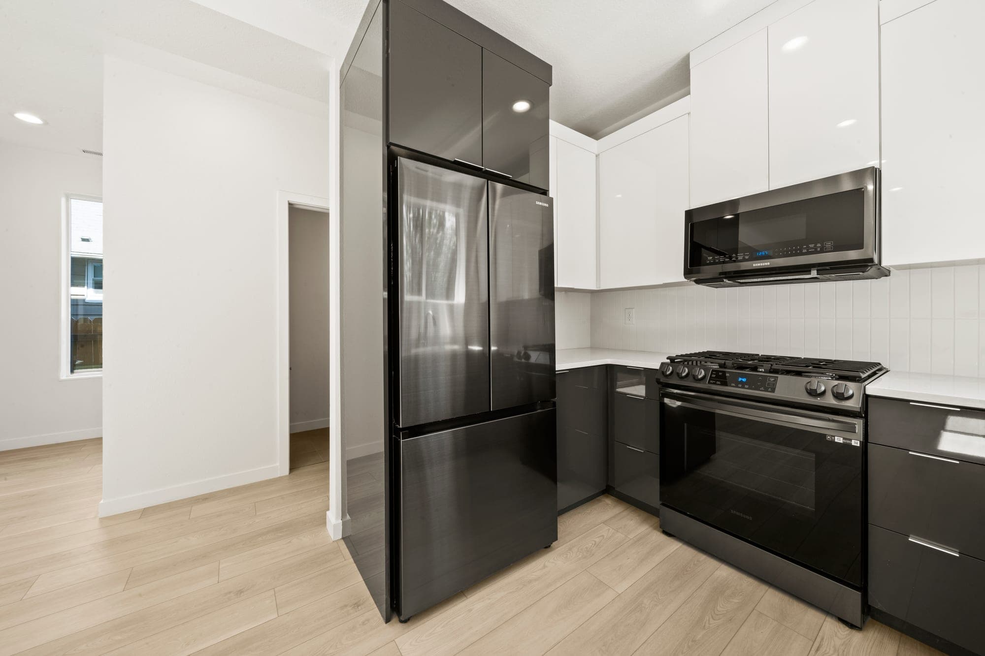 Modern kitchen with charcoal and white high gloss cabinets, slim pulls, stainless steel appliances, quartz counters, a stacked white tile backsplash, and luxury vinyl plank flooring in Northeast Portland, OR