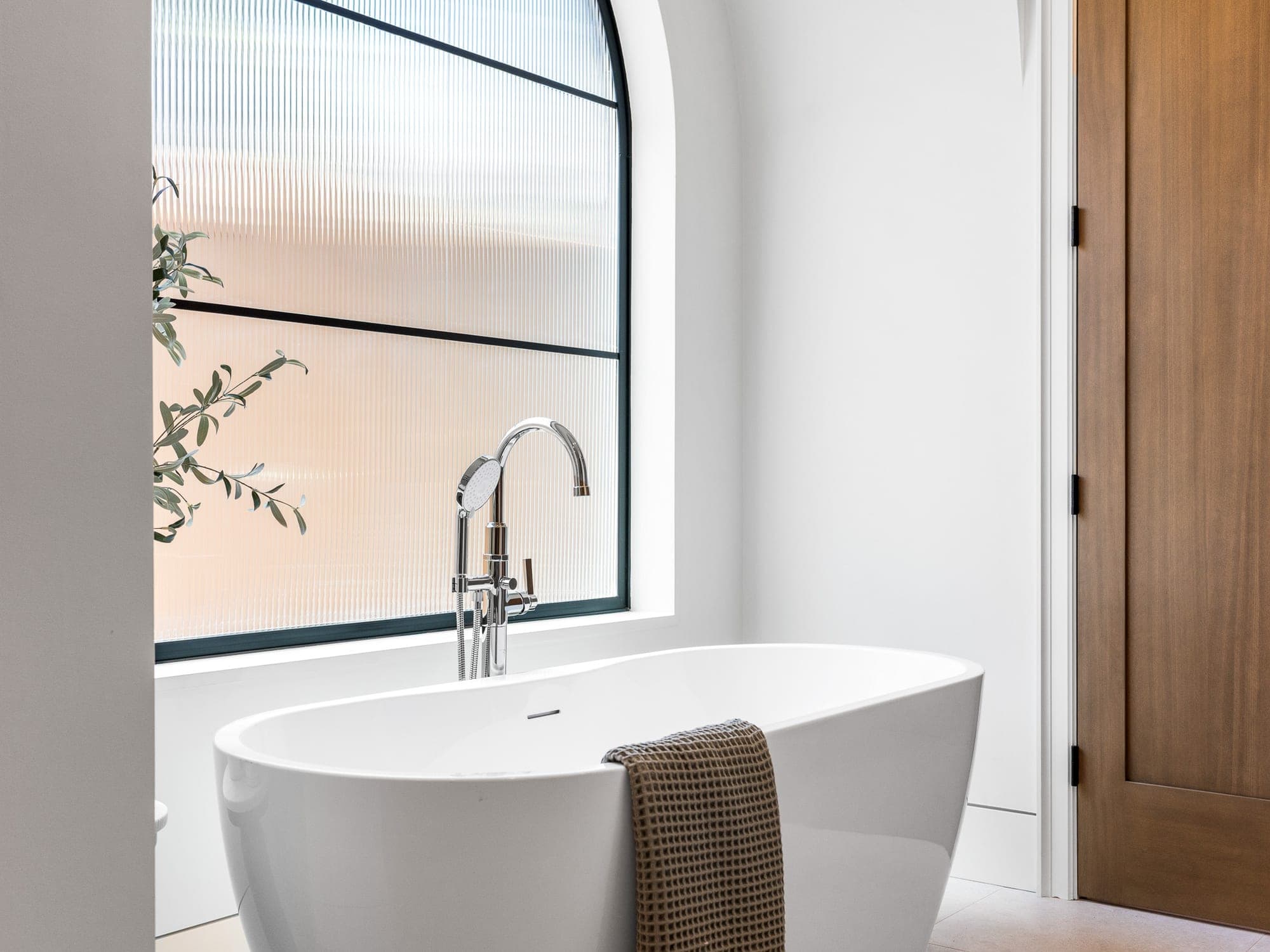 Freestanding tub beneath an arched reeded window with a floor mounted filler in Happy Valley, OR