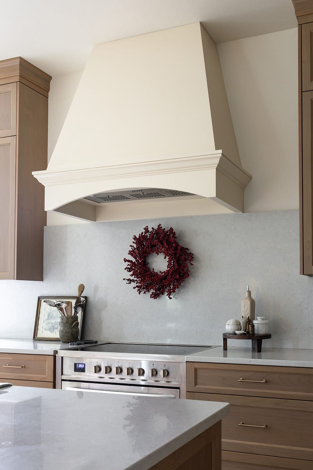 Custom cream plaster range hood over a stainless steel range with a full height quartz backsplash in a white oak kitchen in Camas, WA