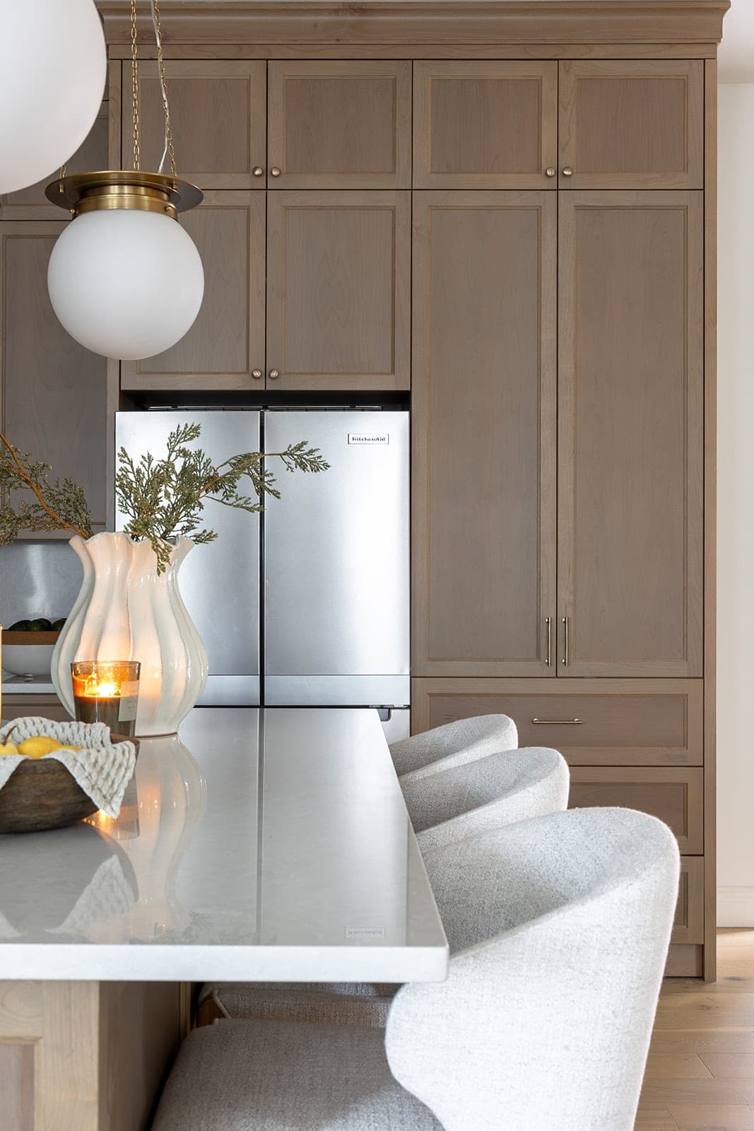 Gold globe pendant, a paneled stainless steel refrigerator, and floor to ceiling white oak cabinetry above a quartz island in Camas, WA