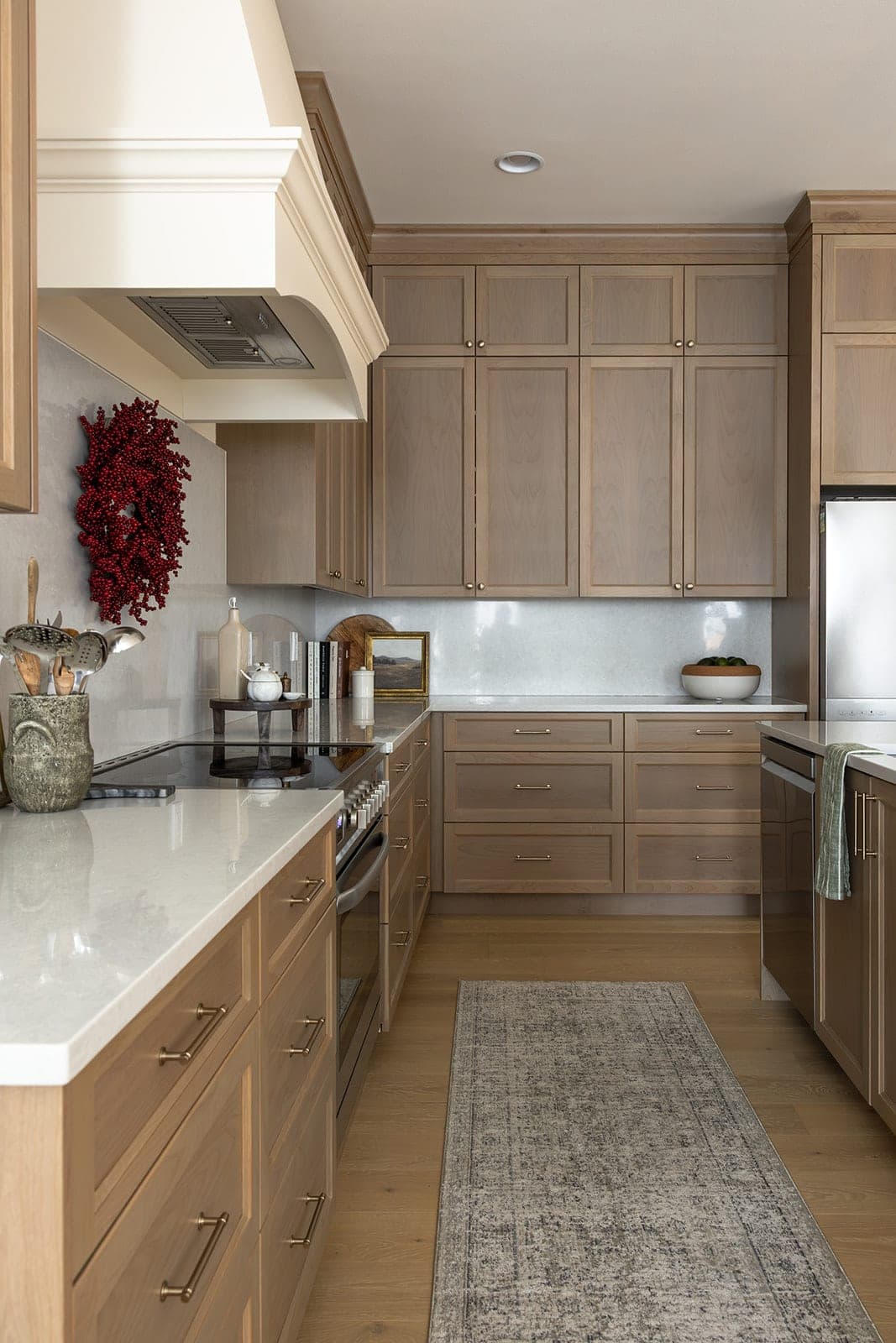 Range wall of a white oak kitchen with a custom hood, gold cabinet pulls, a full height quartz backsplash, and stainless steel appliances in Camas, WA