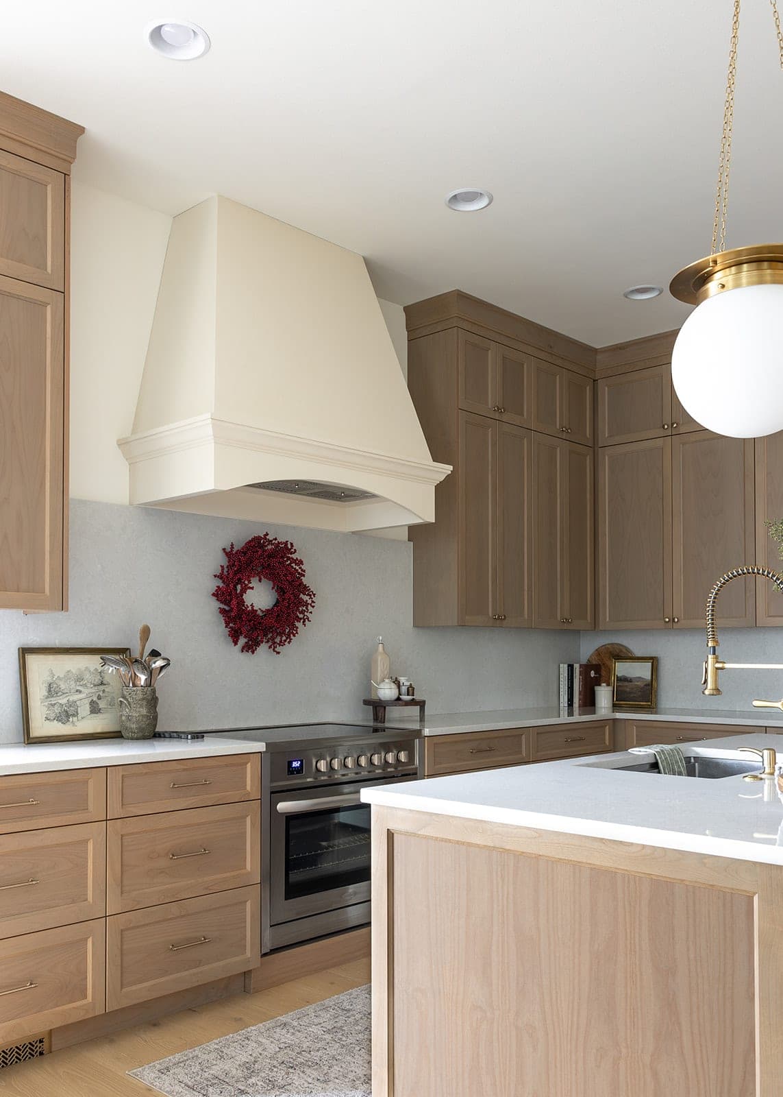 Custom range hood, stainless steel range, and gold globe pendant beside a white oak island with a gold faucet in Camas, WA